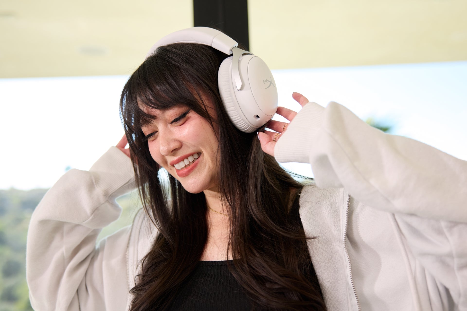 Frau mit weißen Gaming-Kopfhörern und hellem Mantel im Innenbereich