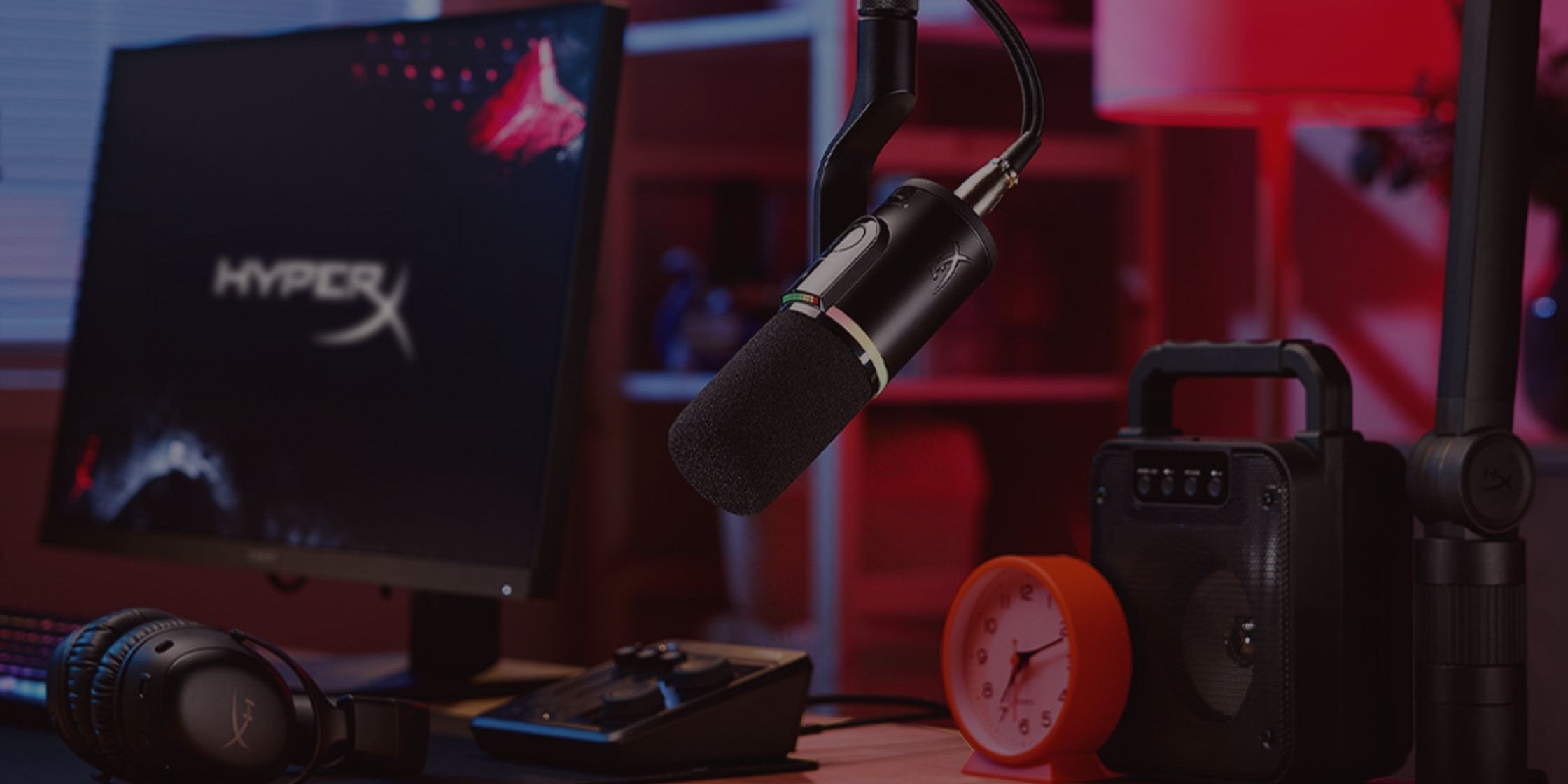 Gaming-Setup mit HyperX-Monitor, Mikrofon und Lautsprechern auf einem Schreibtisch.